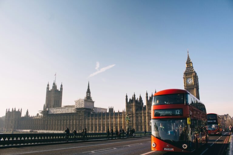 Red double-decker bus crossing Westminster Bridge with Big Ben and the Palace of Westminster in London.
